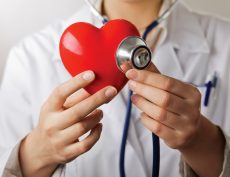 A doctor with stethoscope examining red heart, isolated on white background